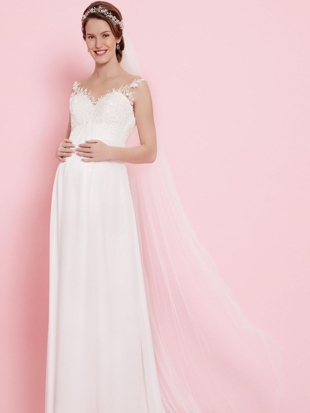 Eine schwangere Frau trägt ein weißes Brautkleid und einen Schleier.