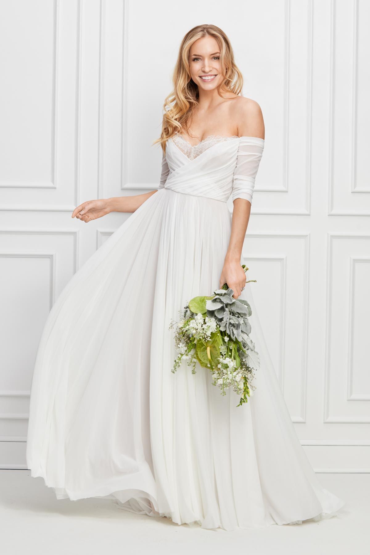 Eine Frau in einem weißen Brautkleid steht vor lila Blumen.