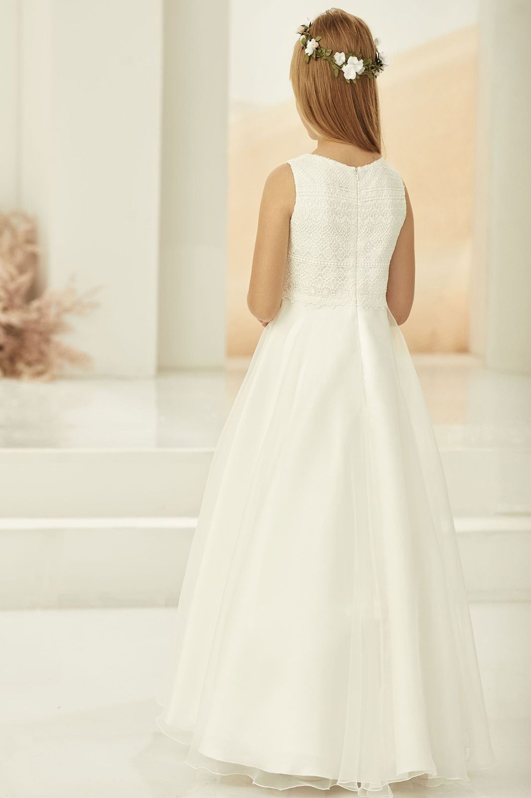 Ein kleines Mädchen trägt ein weißes Kleid und einen Blumenkranz.
