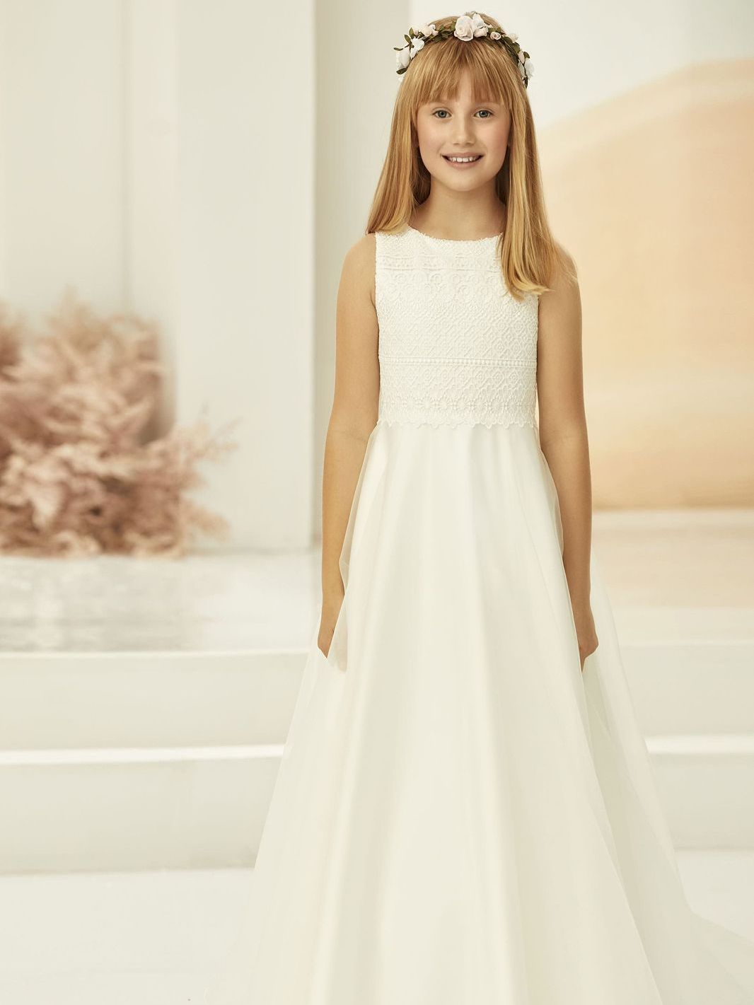 Ein kleines Mädchen trägt ein weißes Kleid und einen Blumenkranz.