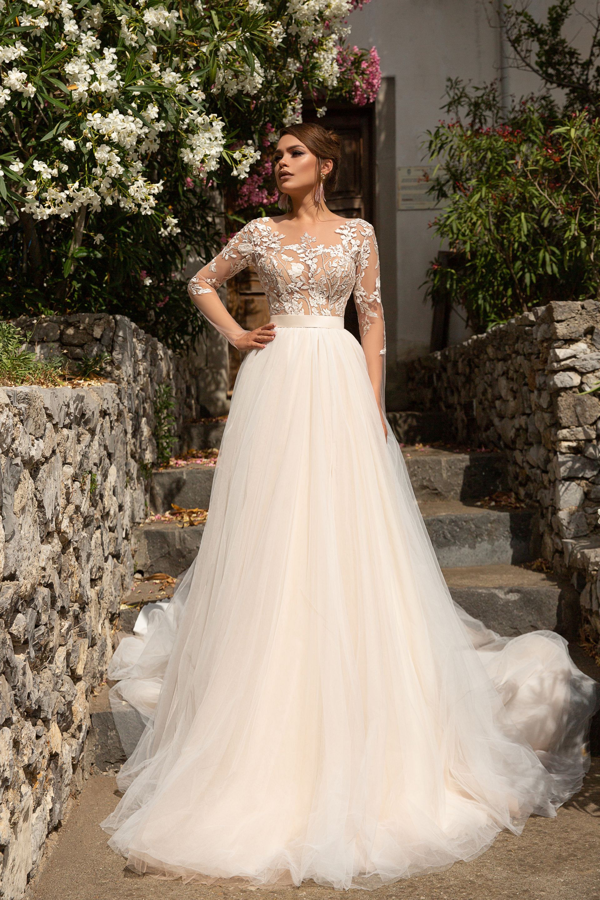 Eine Frau in einem weißen Brautkleid steht vor lila Blumen.