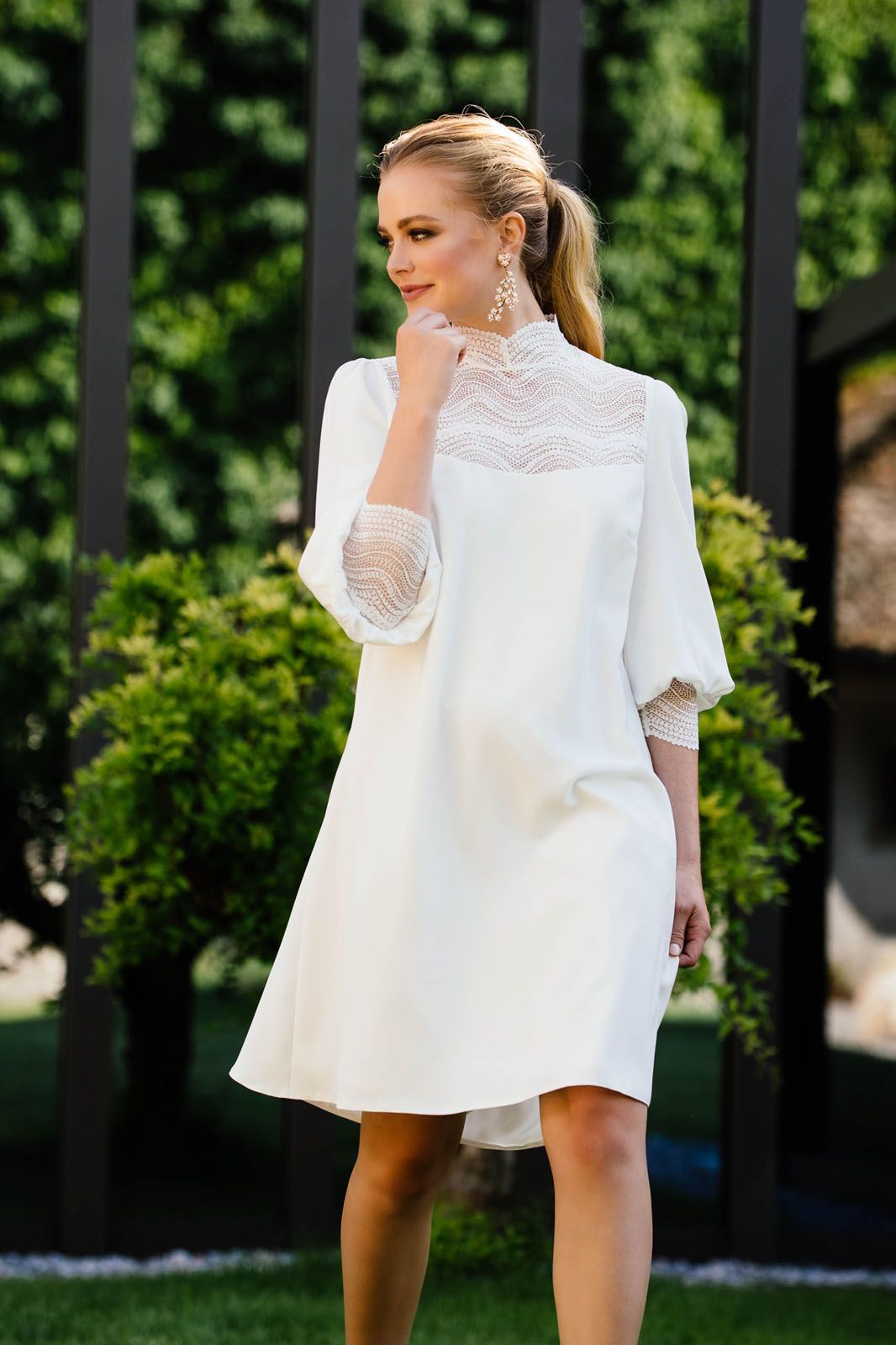 Eine Frau in einem weißen Kleid steht vor einem Zaun.