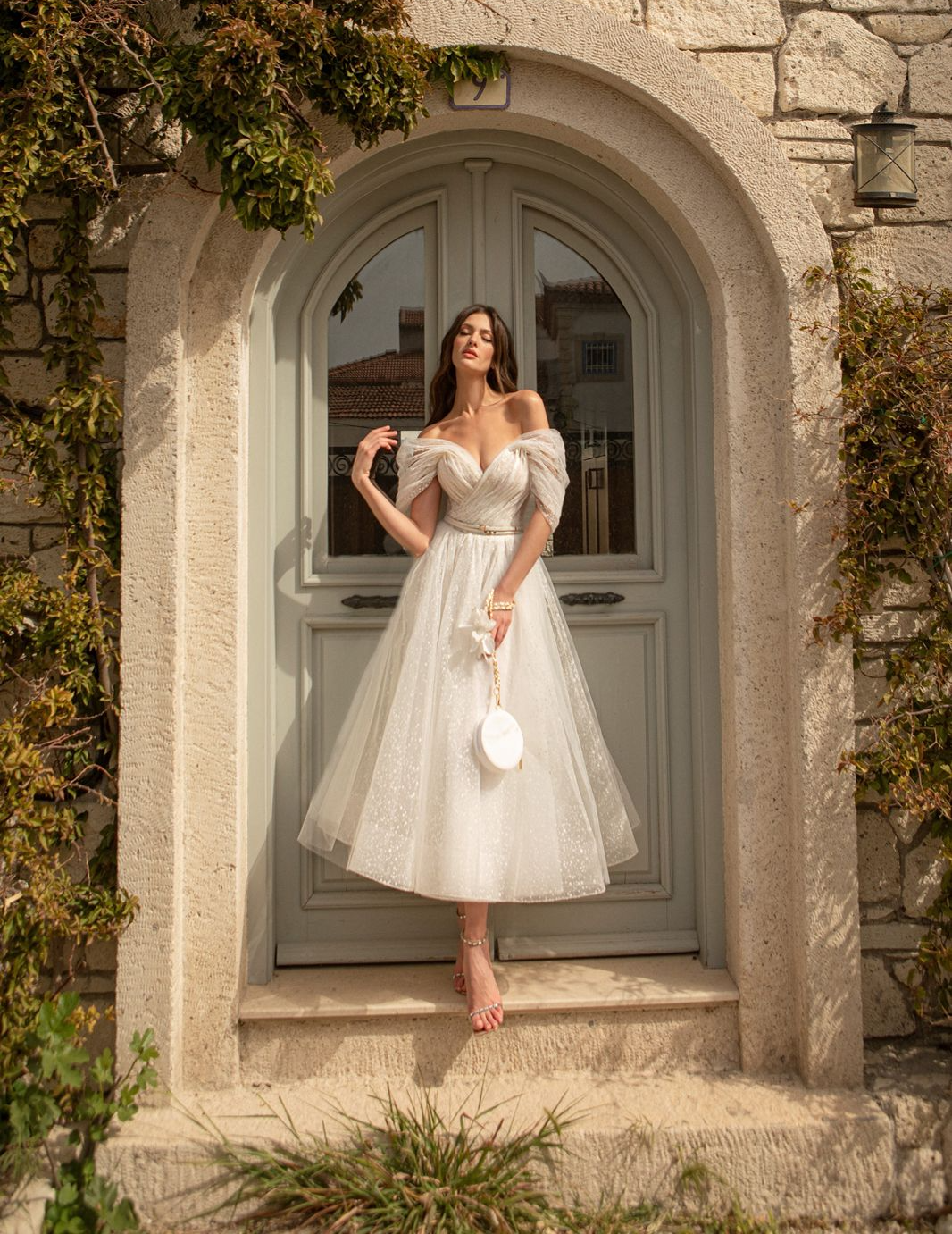 Eine Frau in einem weißen Kleid steht vor einer Tür.