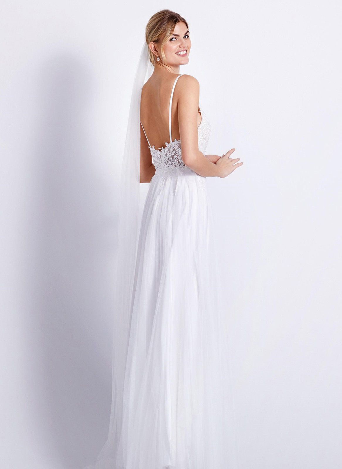 Eine Frau in einem Brautkleid steht vor einer Blumenwand.