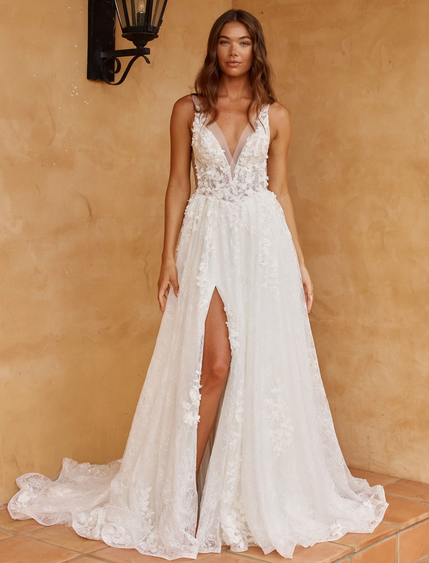 Eine Frau in einem Brautkleid steht vor einer Blumenwand.