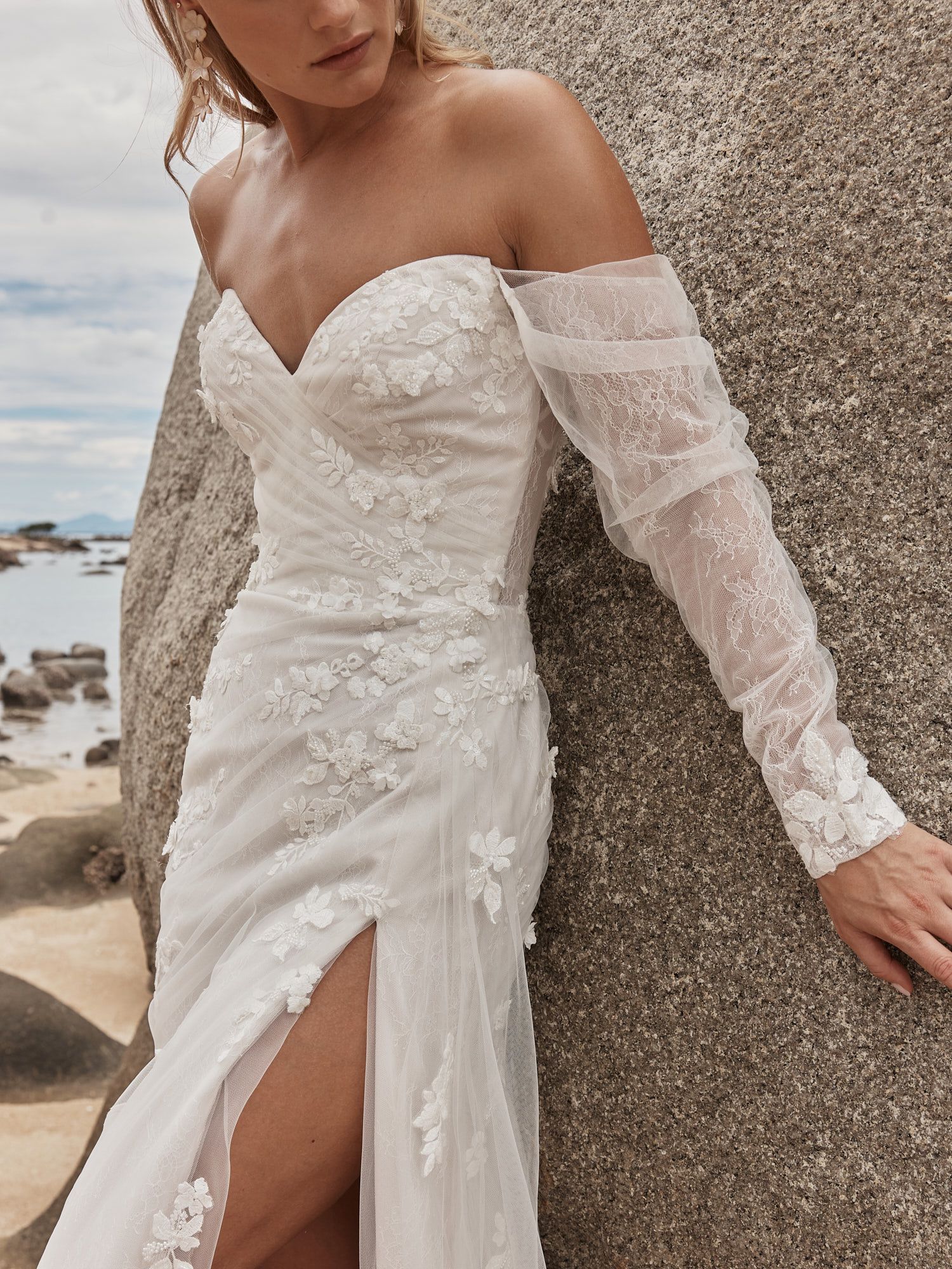 Eine Frau in einem Brautkleid steht an einem steinigen Strand.