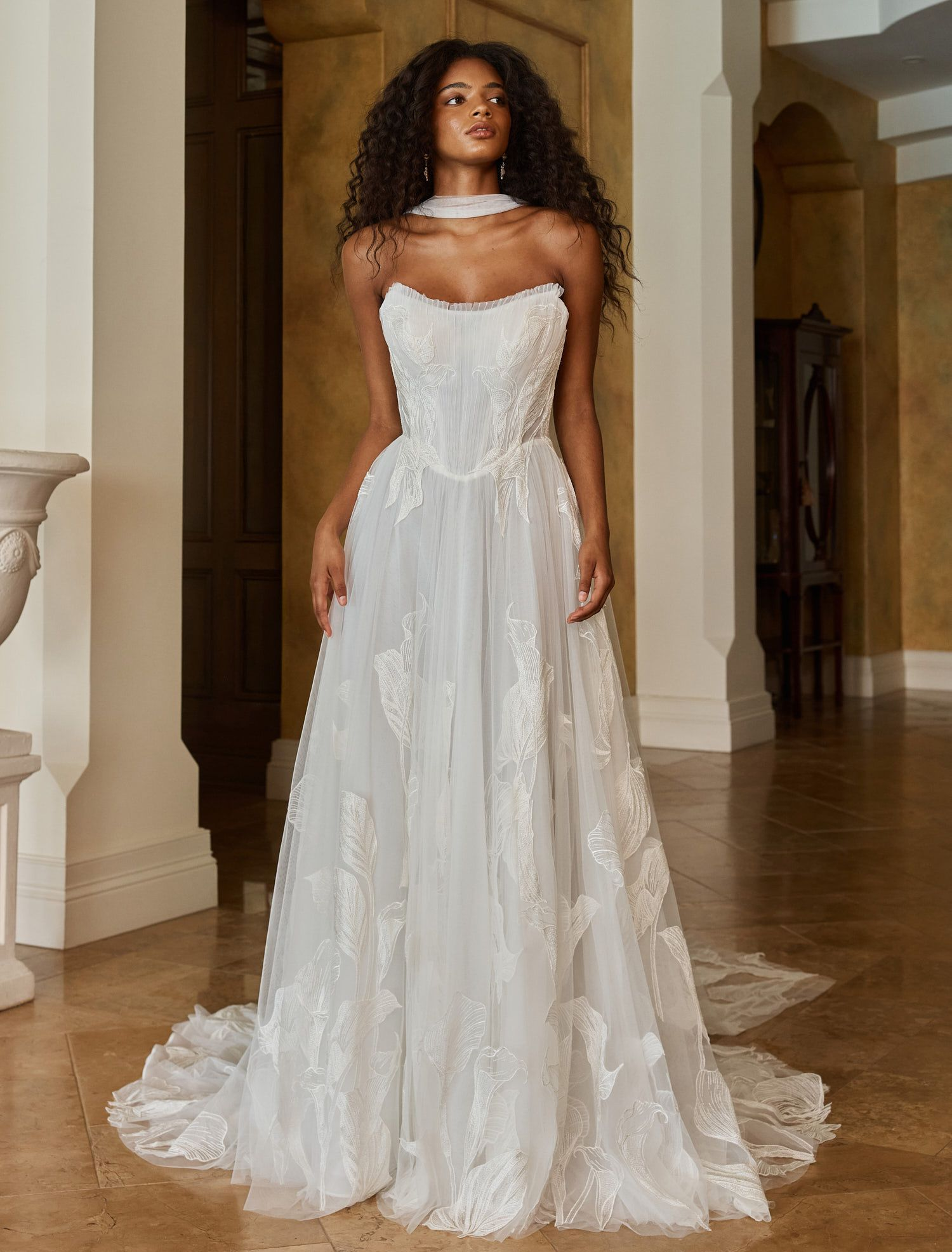 Eine Frau in einem Brautkleid steht vor einer Blumenwand.