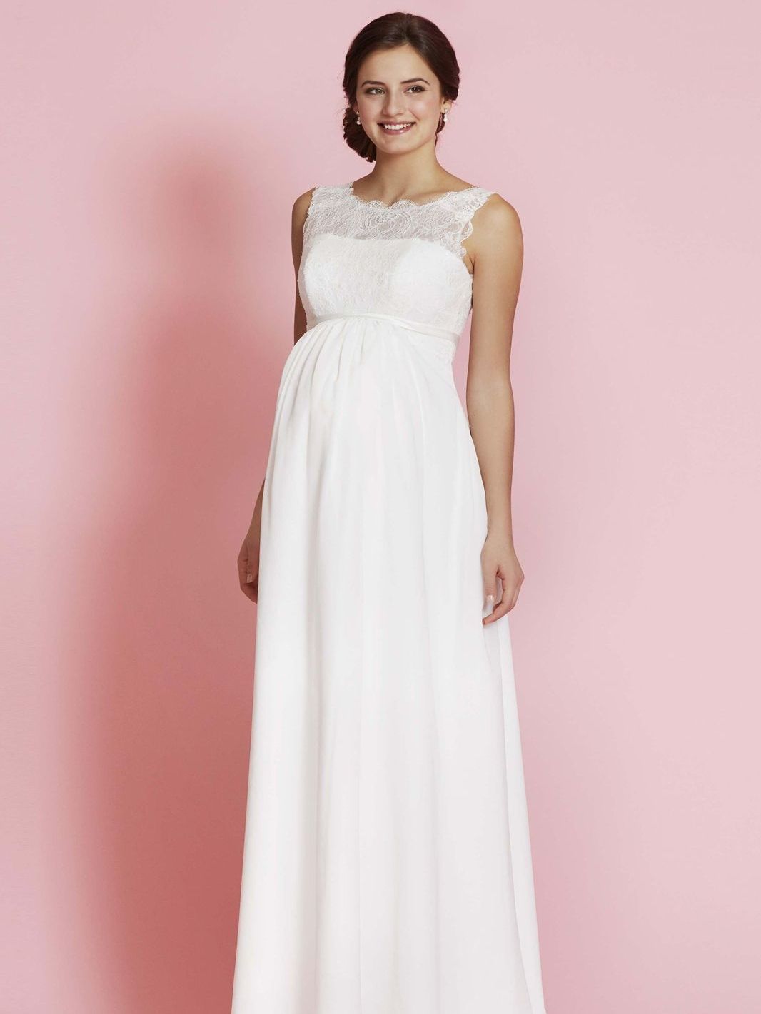 Eine schwangere Frau trägt ein weißes Brautkleid.