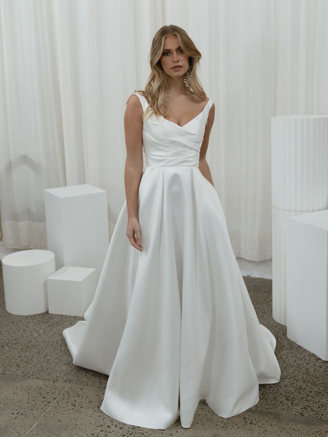Eine Frau in einem weißen Brautkleid steht in einem Raum mit weißen Würfeln.