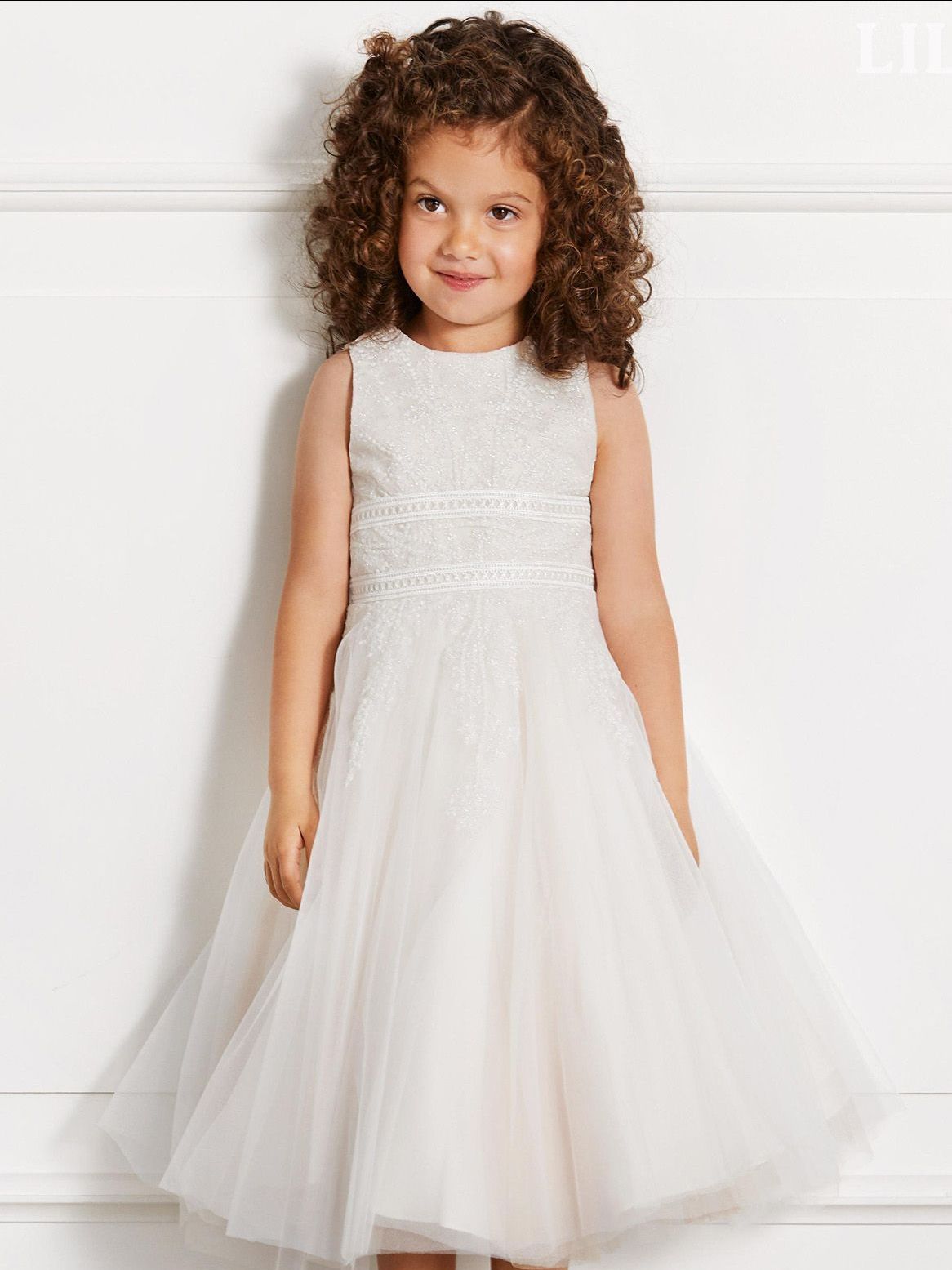 Ein kleines Mädchen mit lockigem Haar trägt ein weißes Kleid.