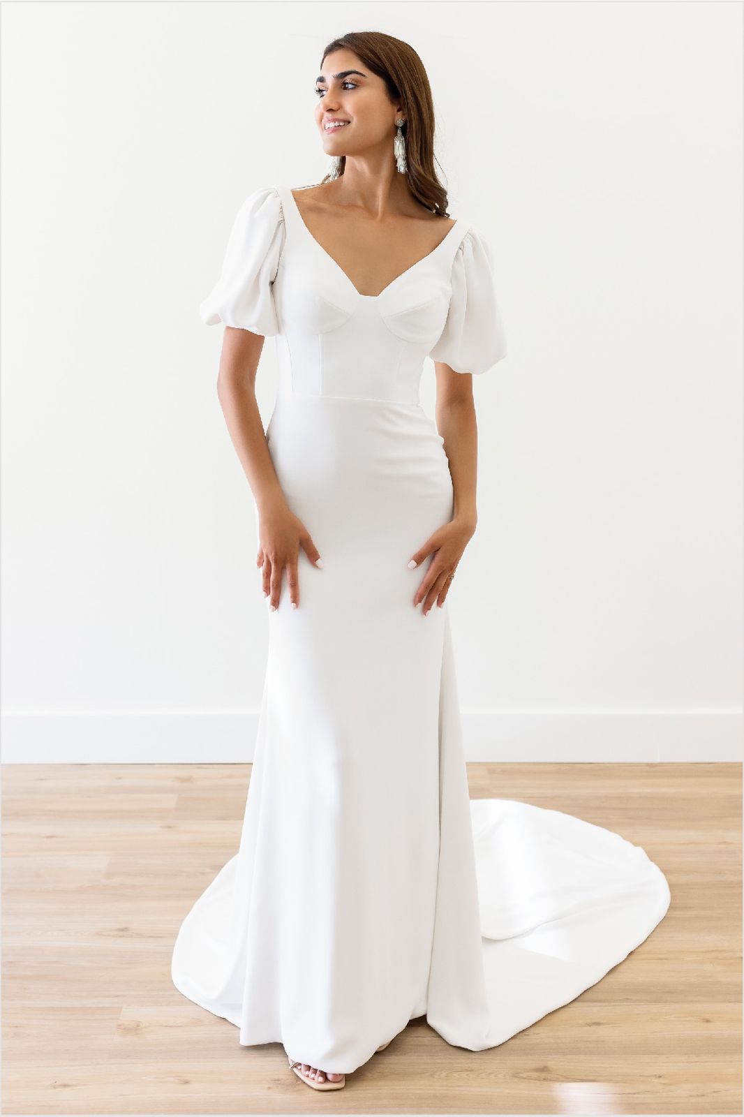 Eine Frau in einem weißen Brautkleid steht vor lila Blumen.