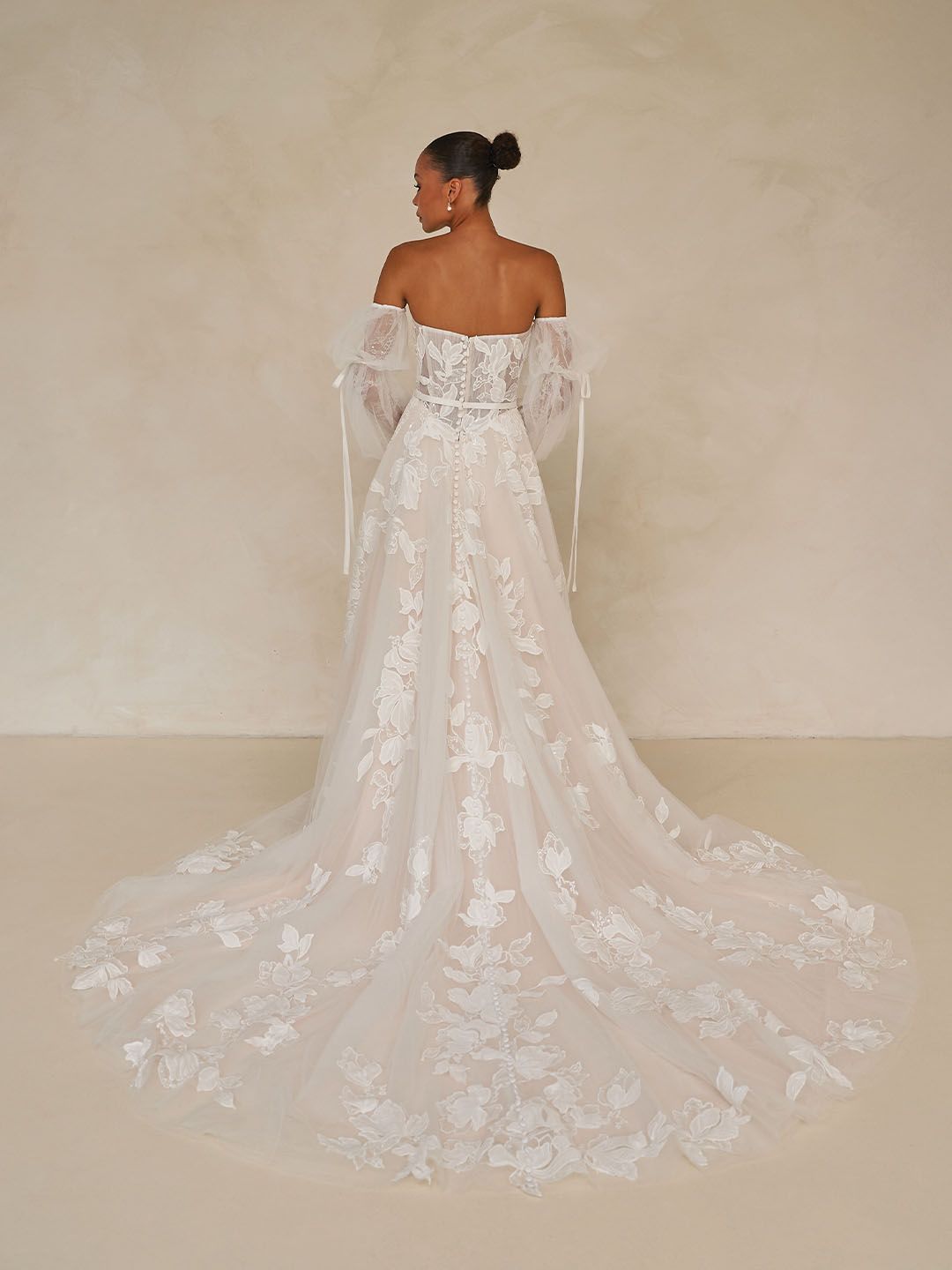 Eine Frau in einem Brautkleid steht vor einer Blumenwand.