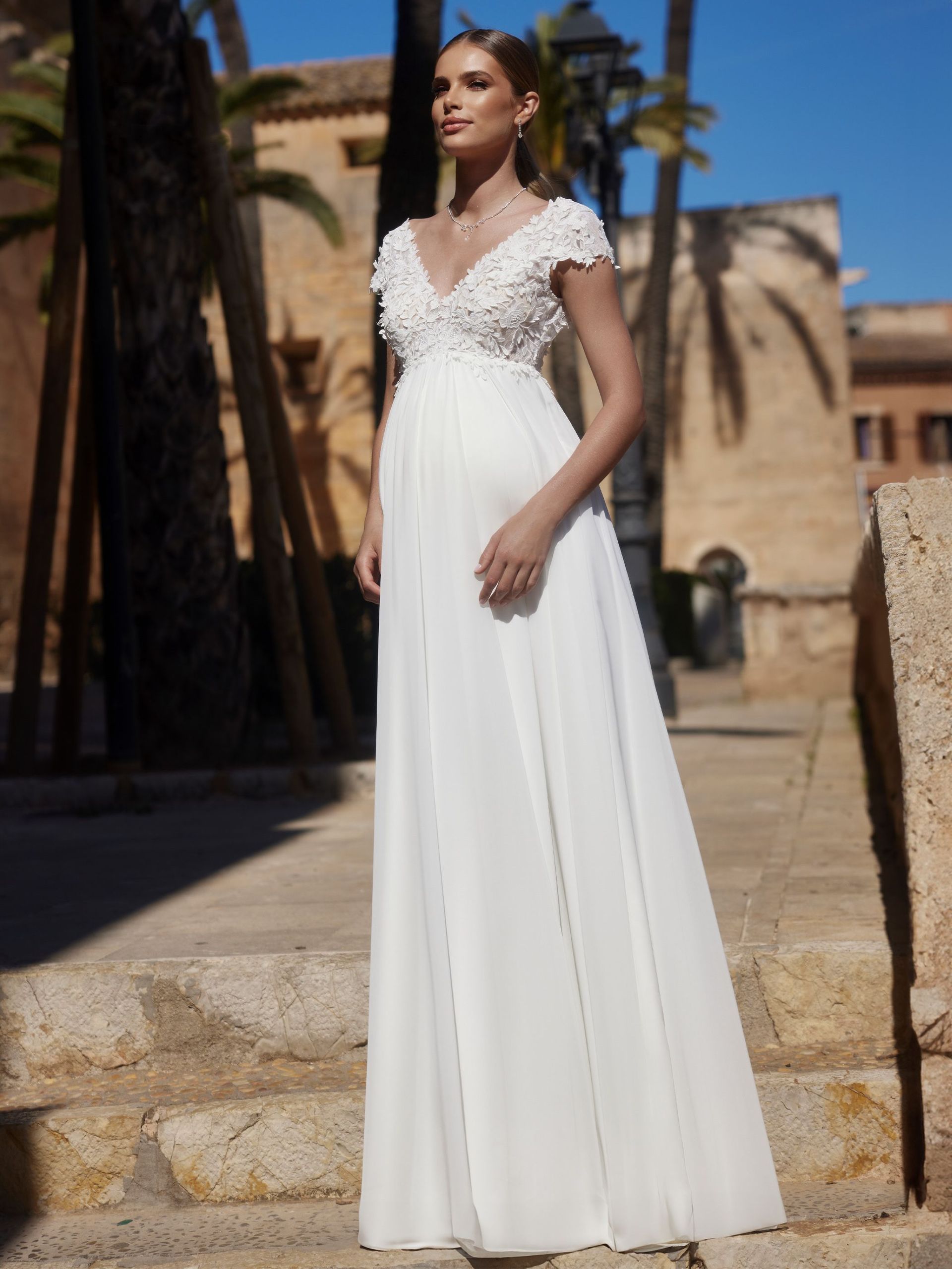 Eine schwangere Frau trägt ein weißes Brautkleid.