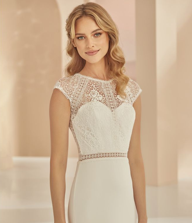 Eine Frau in einem weißen Kleid steht vor Blumen.