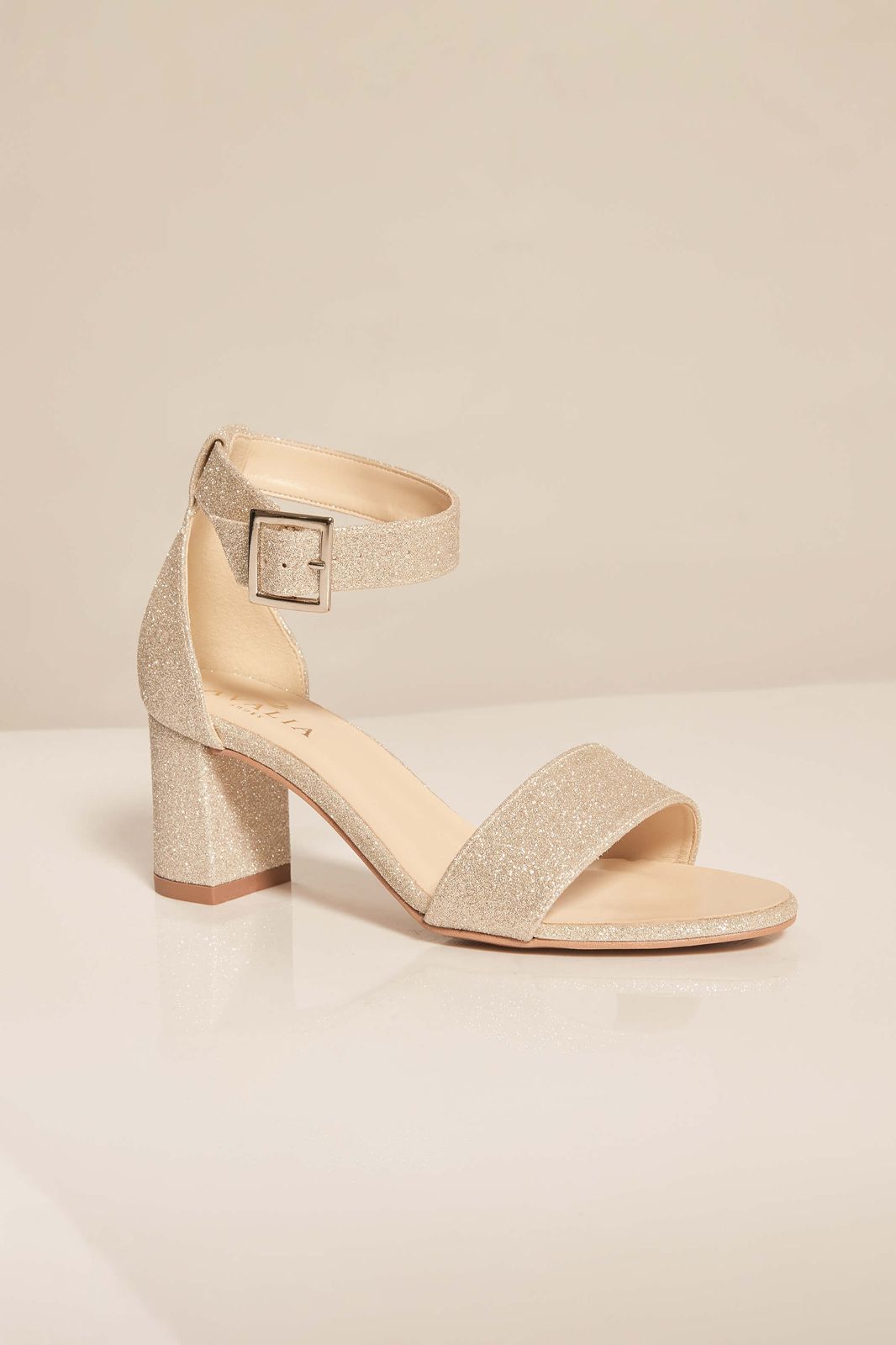Ein Paar goldene Sandalen mit einer Schnalle um den Knöchel auf einem Tisch.