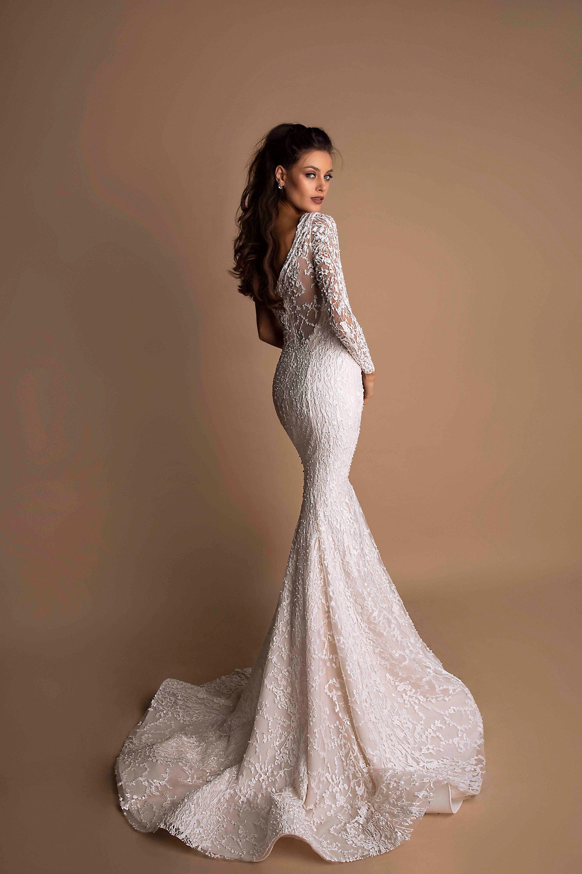 Eine Frau trägt ein weißes Brautkleid mit langen Ärmeln und einer Schleppe.