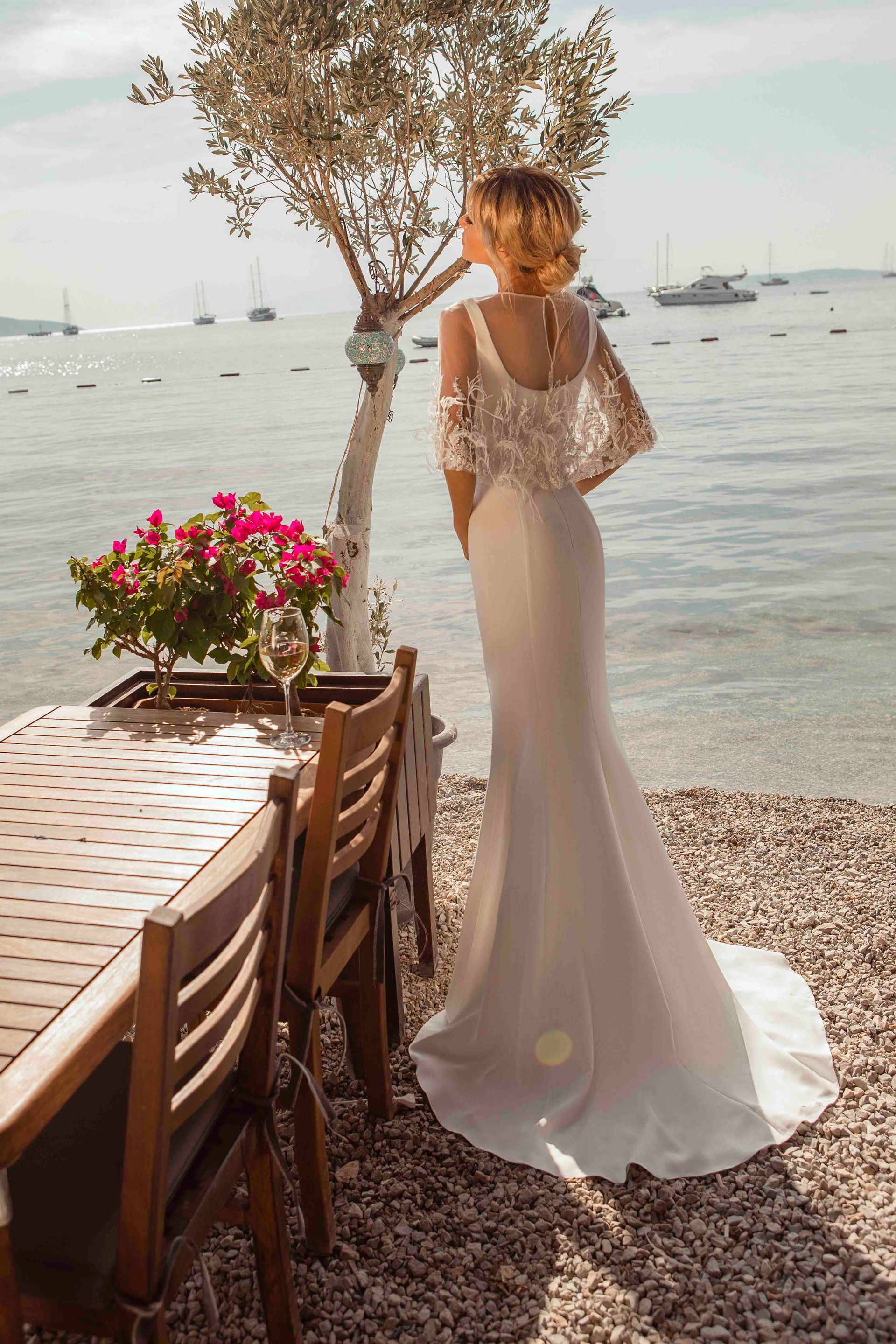 Eine Frau in einem Brautkleid steht neben einem Tisch und Stühlen am Strand.
