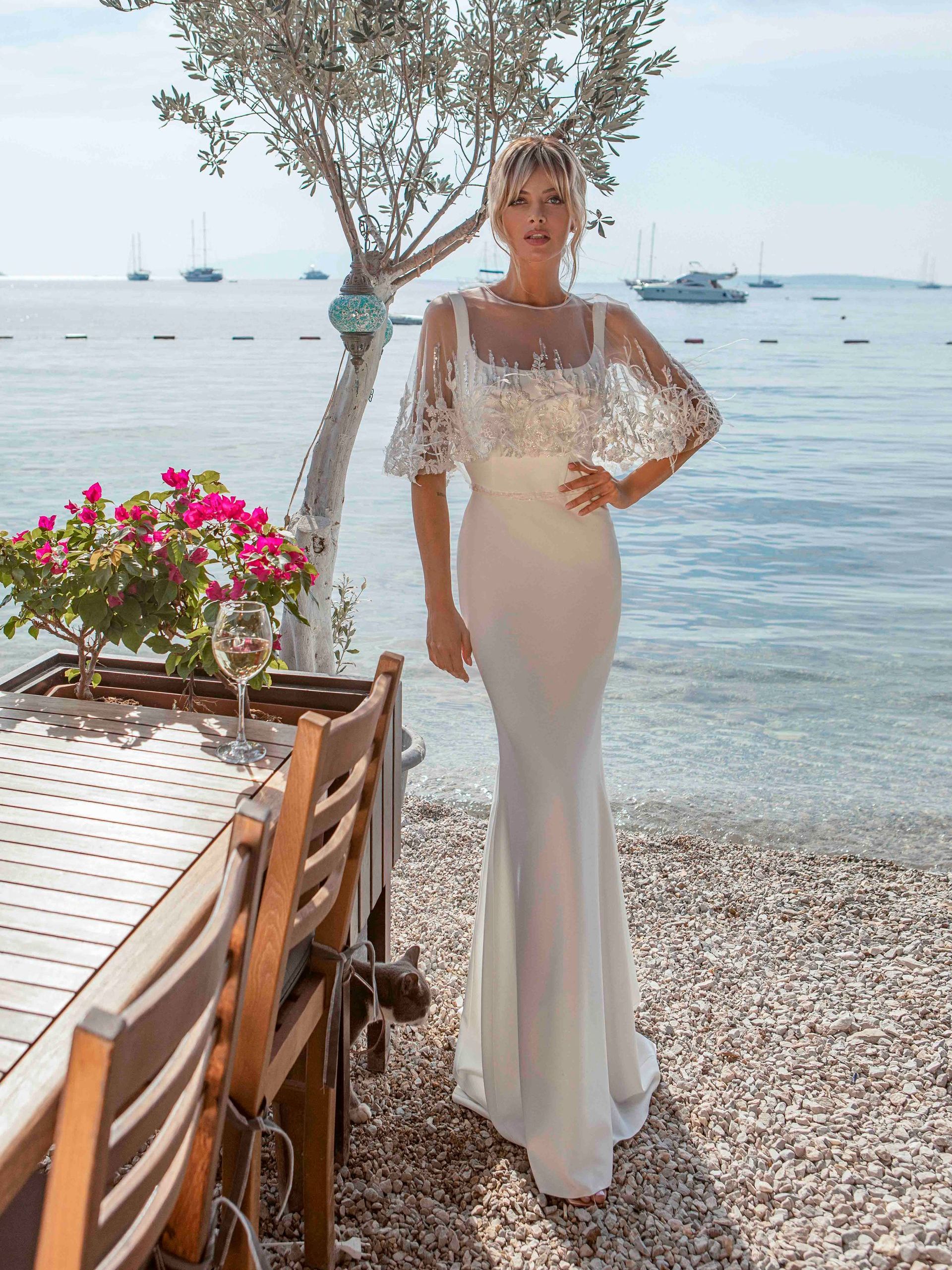 Eine Frau in einem Brautkleid steht neben einem Tisch und Stühlen am Strand.