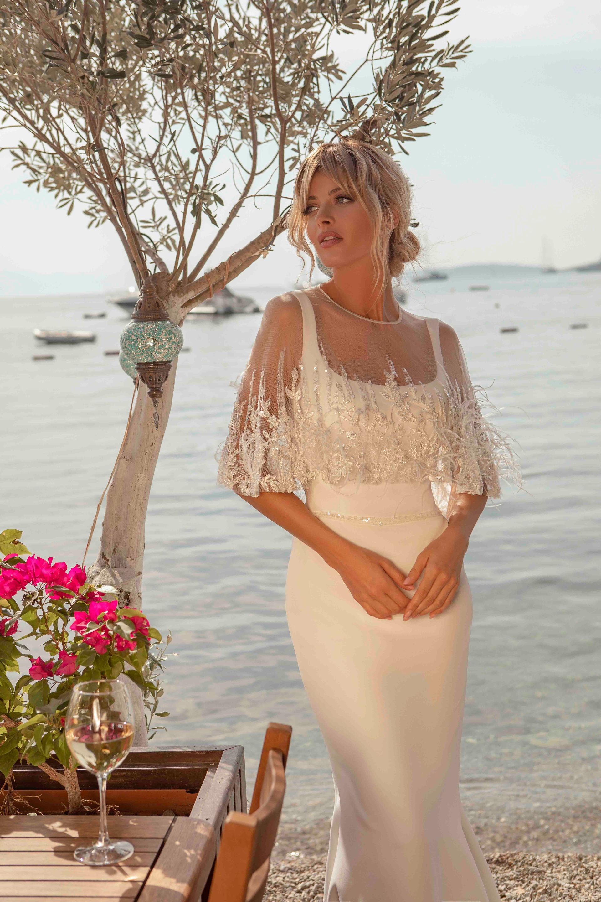 Eine Frau in einem Brautkleid steht mit einem Glas Wein neben einem Tisch.