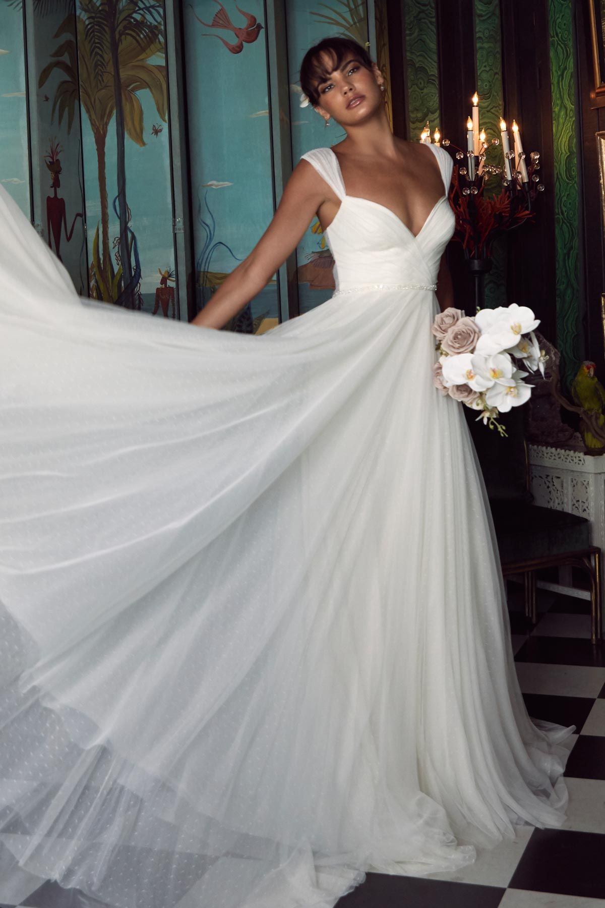 Eine Frau in einem weißen Brautkleid steht vor lila Blumen.