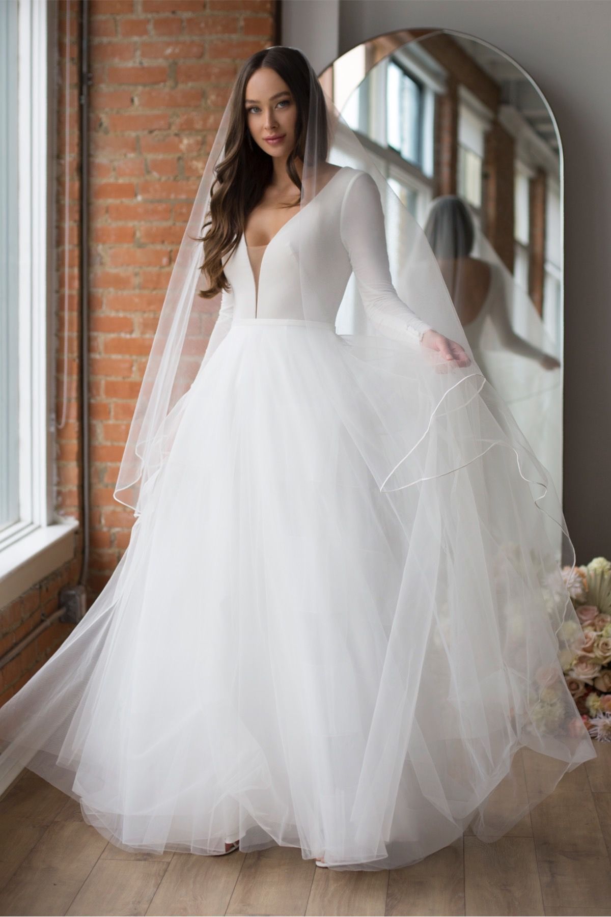 Eine Frau in einem weißen Brautkleid steht vor lila Blumen.