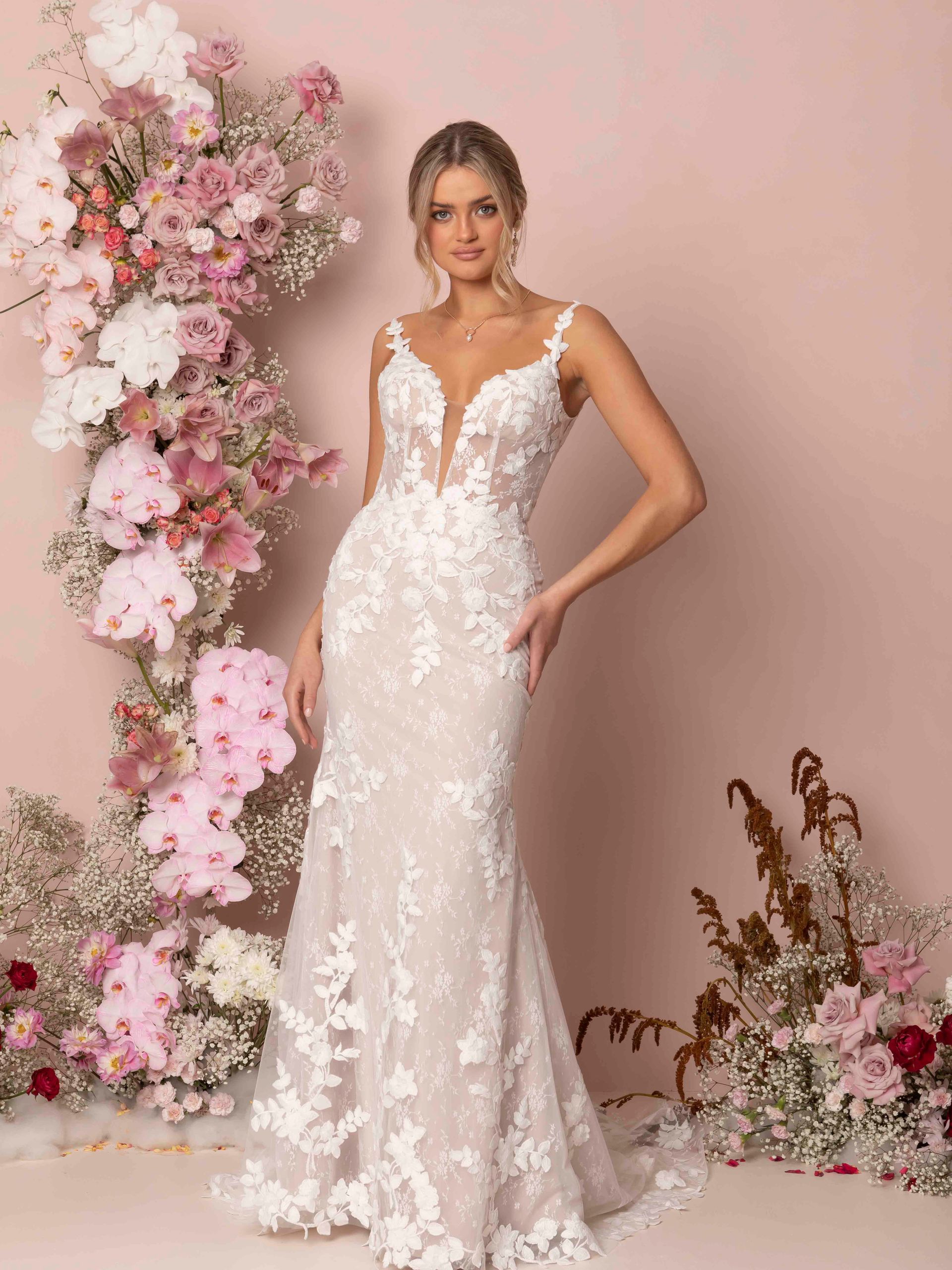 Eine Frau in einem Brautkleid steht vor einer Wand aus rosa Blumen.