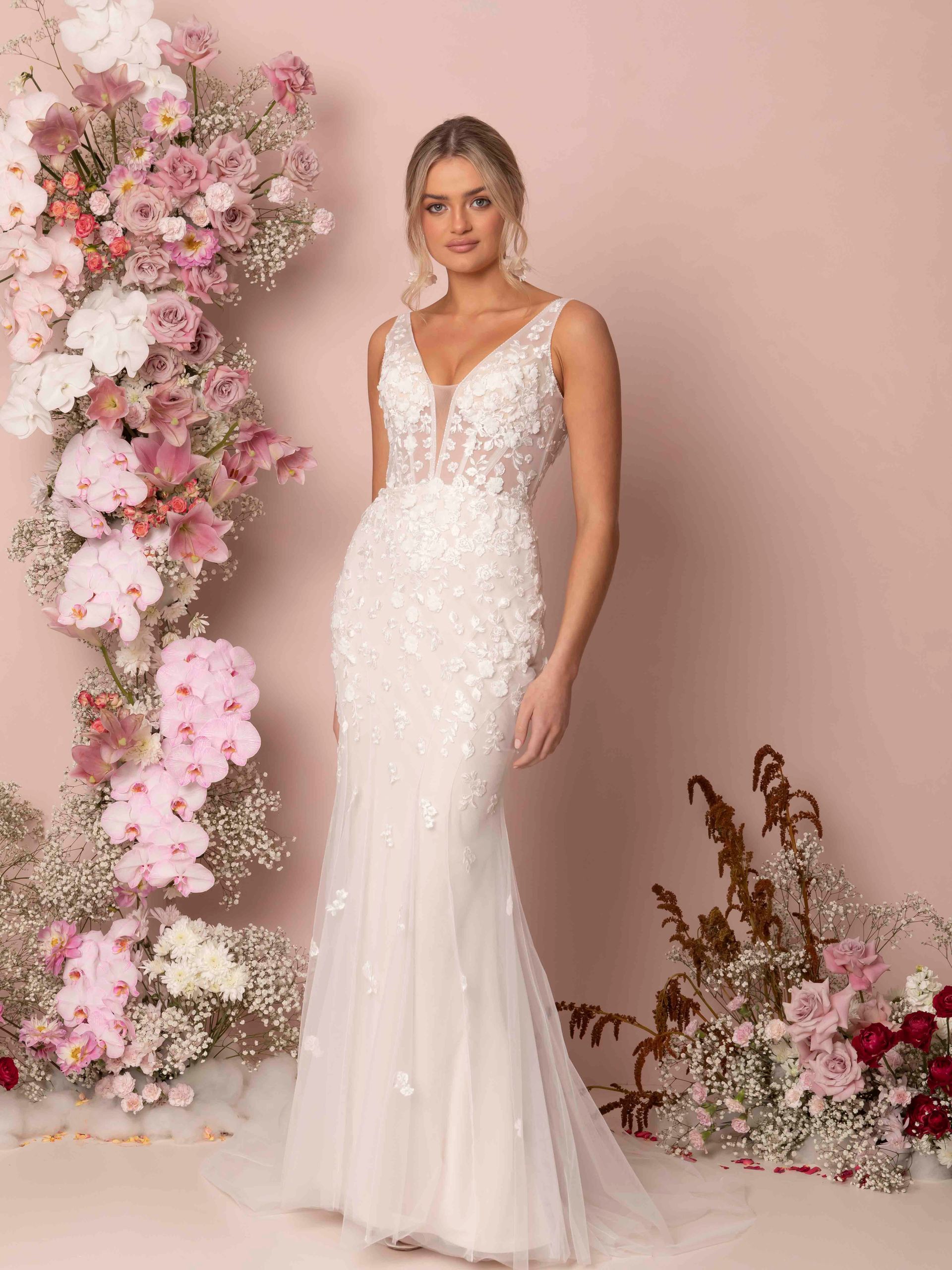 Eine Frau in einem Brautkleid steht vor einer Blumenwand.