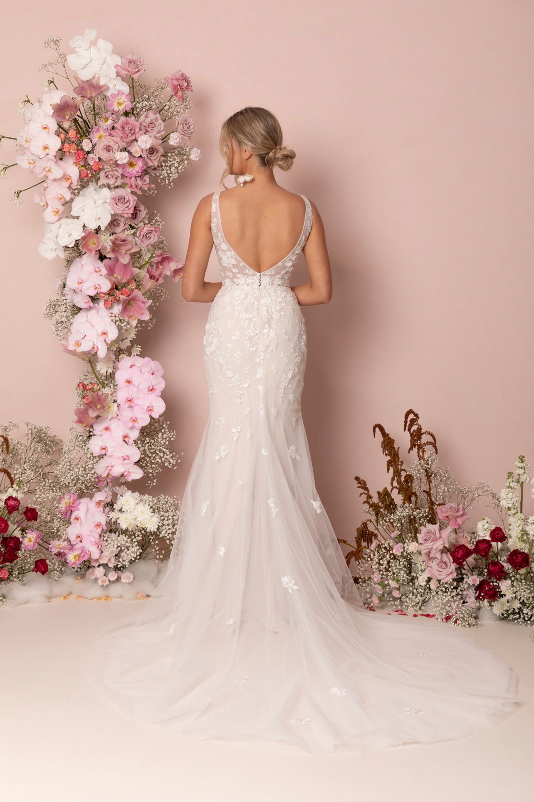 Eine Frau in einem Brautkleid steht vor einer Blumenwand.