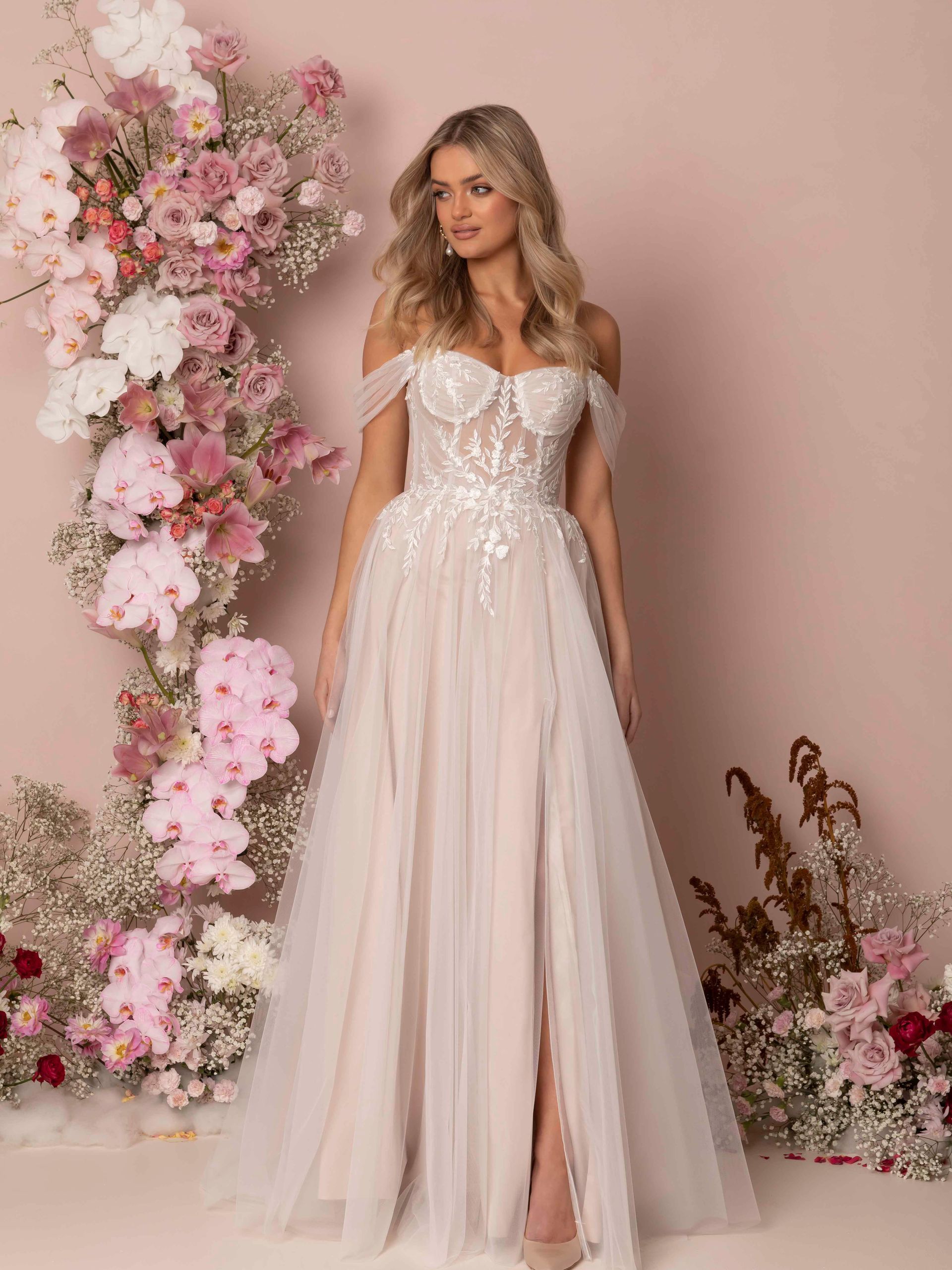 Eine Frau in einem Brautkleid steht vor einer Wand aus rosa Blumen.