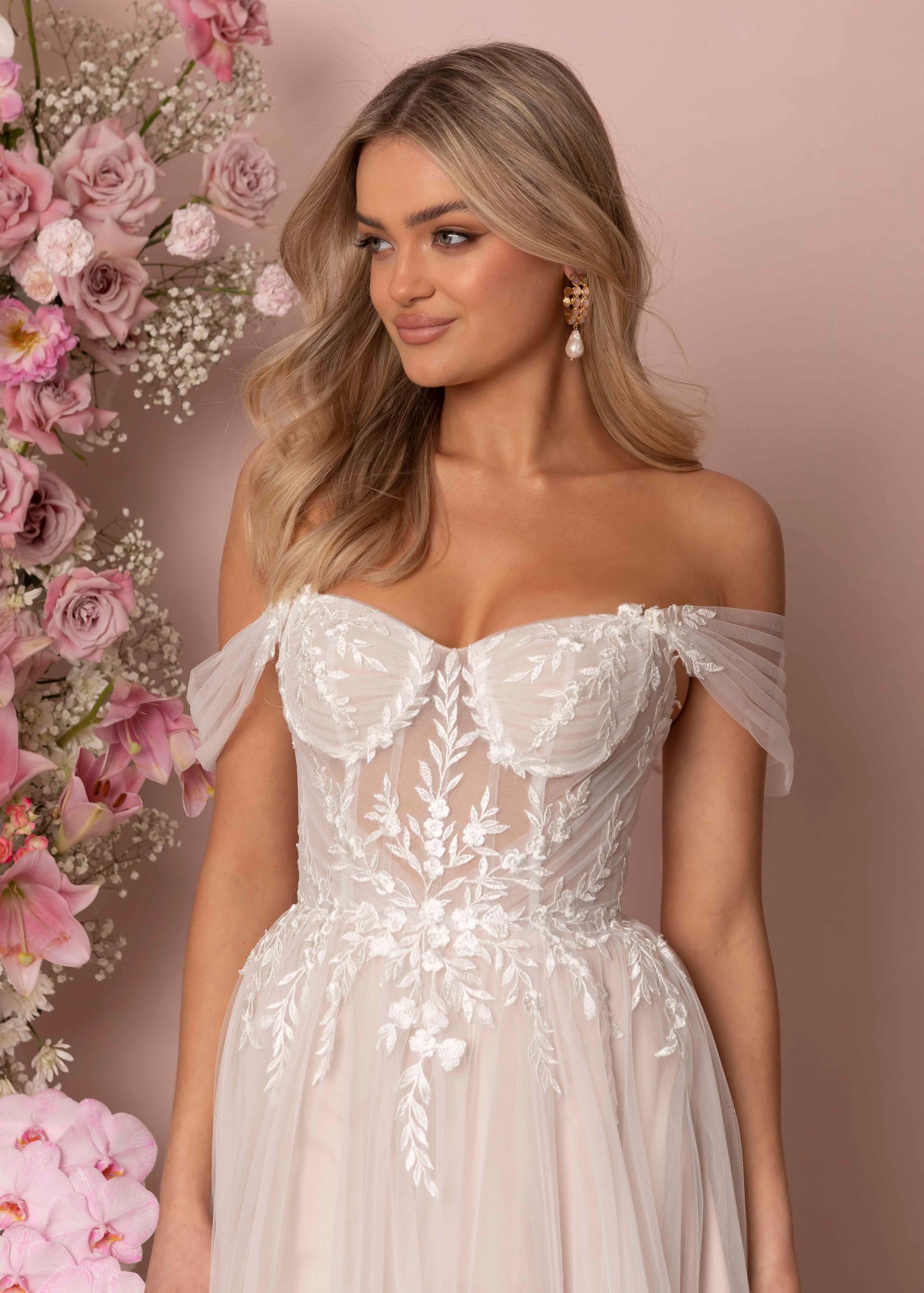 Eine Frau in einem weißen Brautkleid steht vor Blumen.