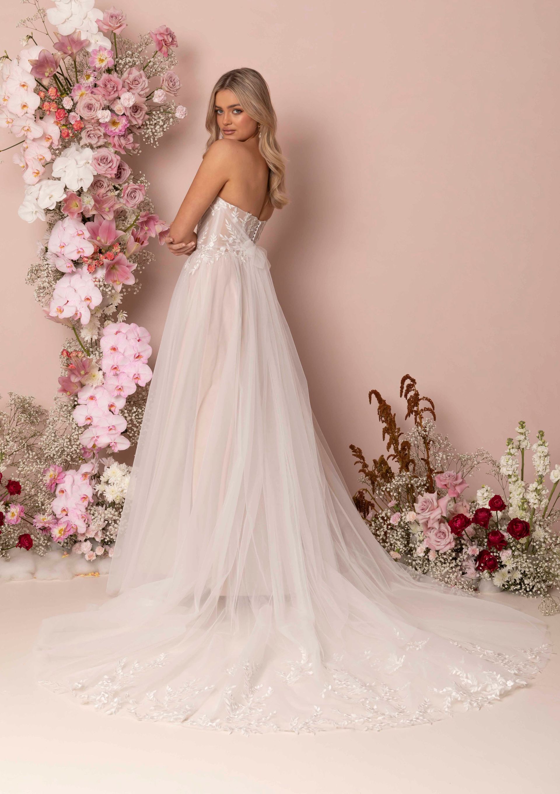 Eine Frau in einem Brautkleid steht vor einer Blumenwand.