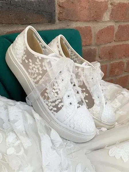 Ein Paar weiße Spitzen-Sneakers liegen auf einem weißen Tuch