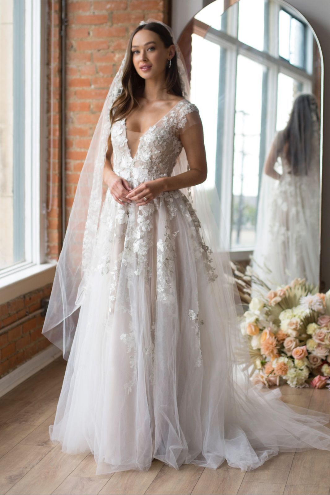 Eine Frau in einem weißen Brautkleid steht vor lila Blumen.