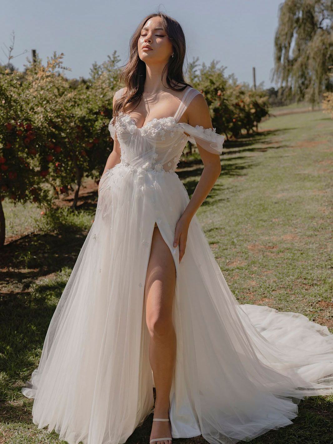 Eine Frau in einem weißen Brautkleid steht im Gras.