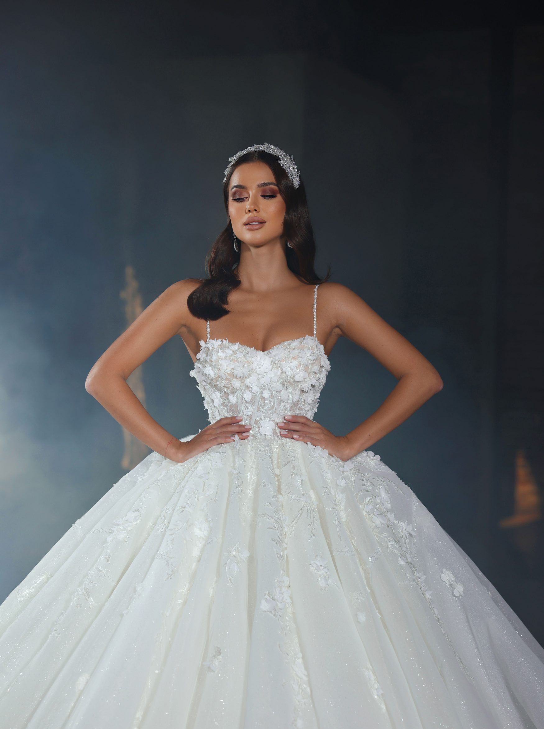 Eine Frau in einem weißen Ballkleid steht mit den Händen in den Hüften da.