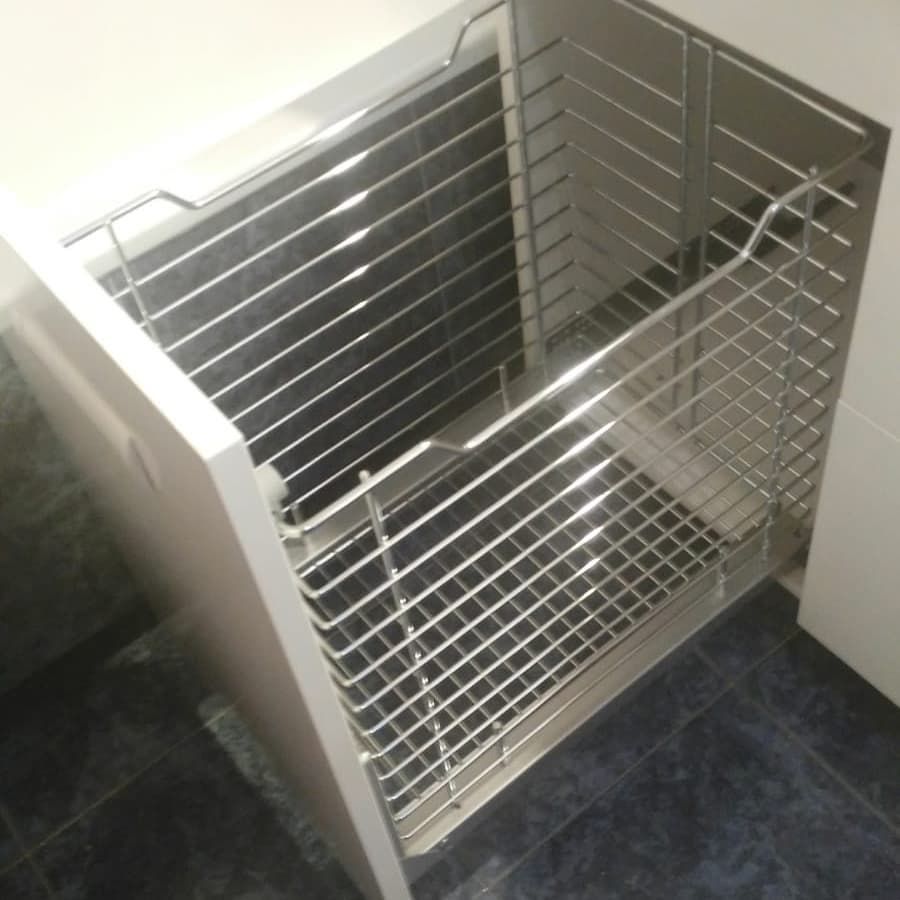 Cesta de alambre de acero inoxidable abierta instalada en un gabinete blanco.