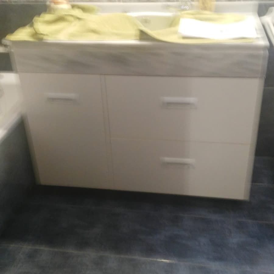 Mueble de baño con gabinetes blancos, encimera clara y piso azul oscuro.