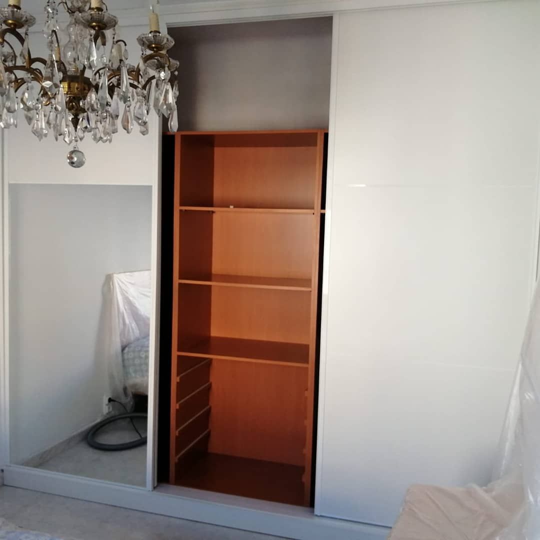 Armario con puertas corredizas blancas y una estantería marrón entre ellas. 