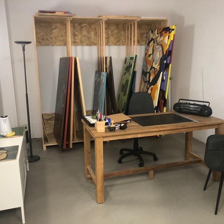 Estudio de arte con escritorio, cuadros, estanterías de almacenaje y muebles minimalistas.