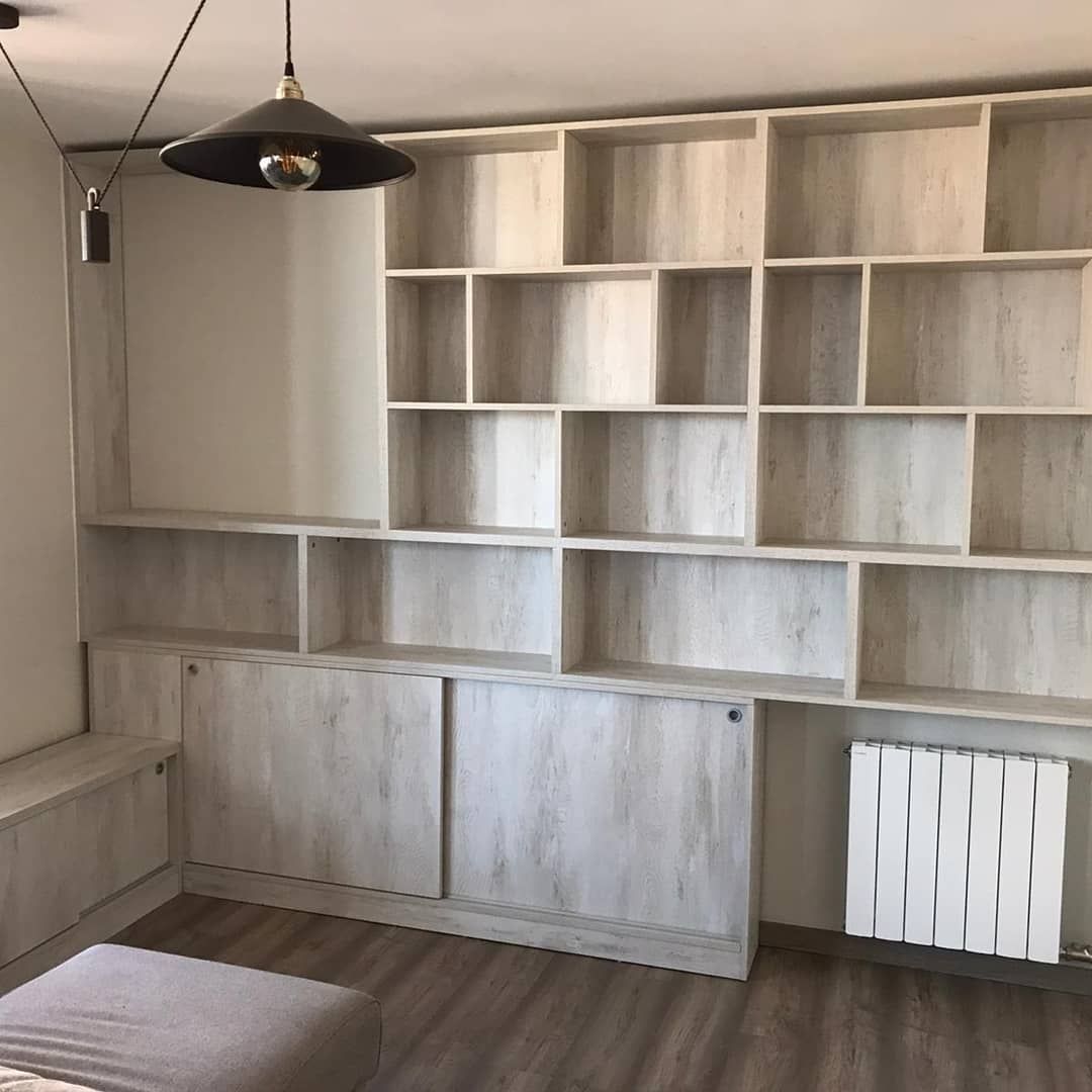 Estantería de madera empotrada contra la pared, con armarios y estantes abiertos. Acabado blanco grisáceo. Diseño moderno.