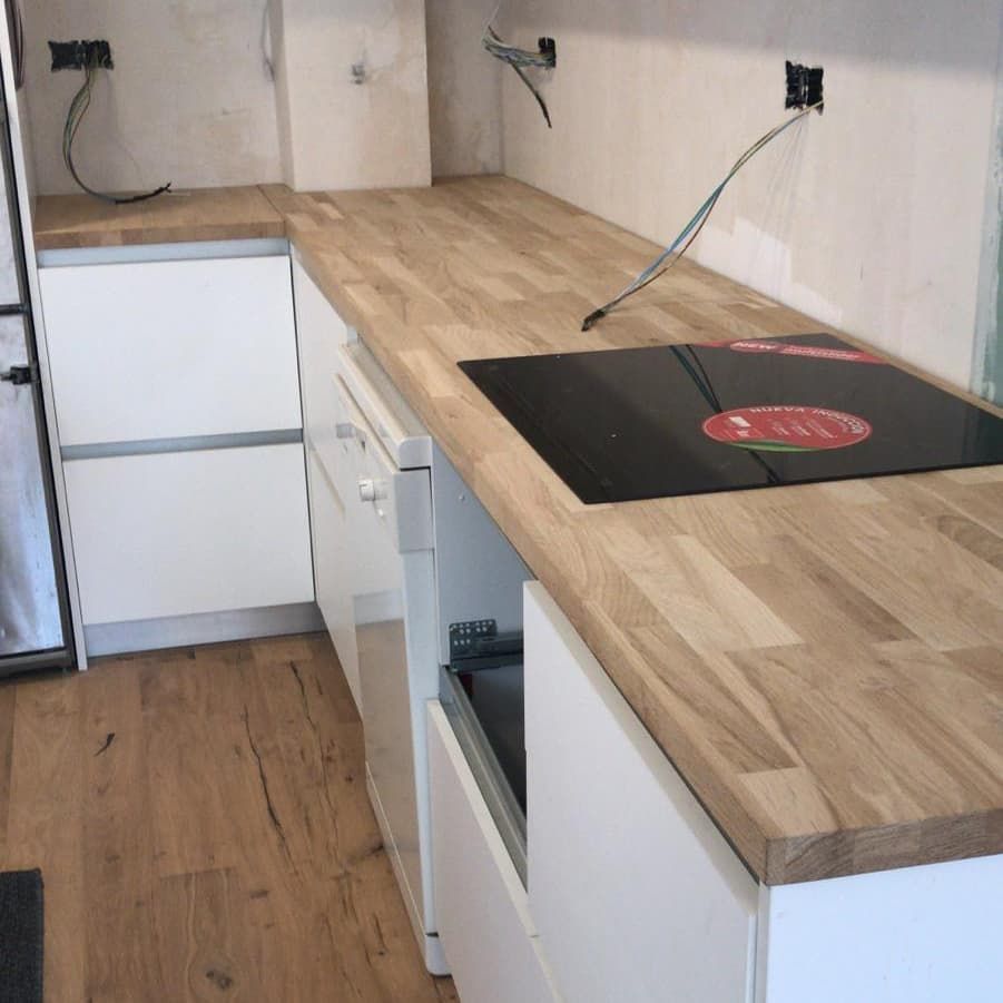 Gabinetes de cocina blancos con encimera de madera, anafe incorporado y cableado eléctrico.