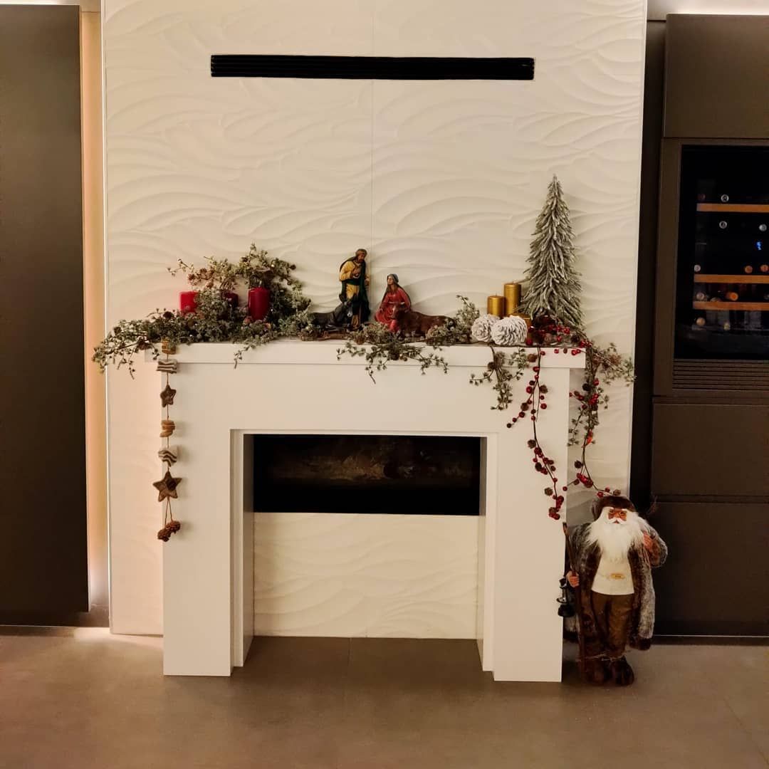Chimenea blanca decorada con guirnalda navideña, velas y figuras, frente a pared texturizada.