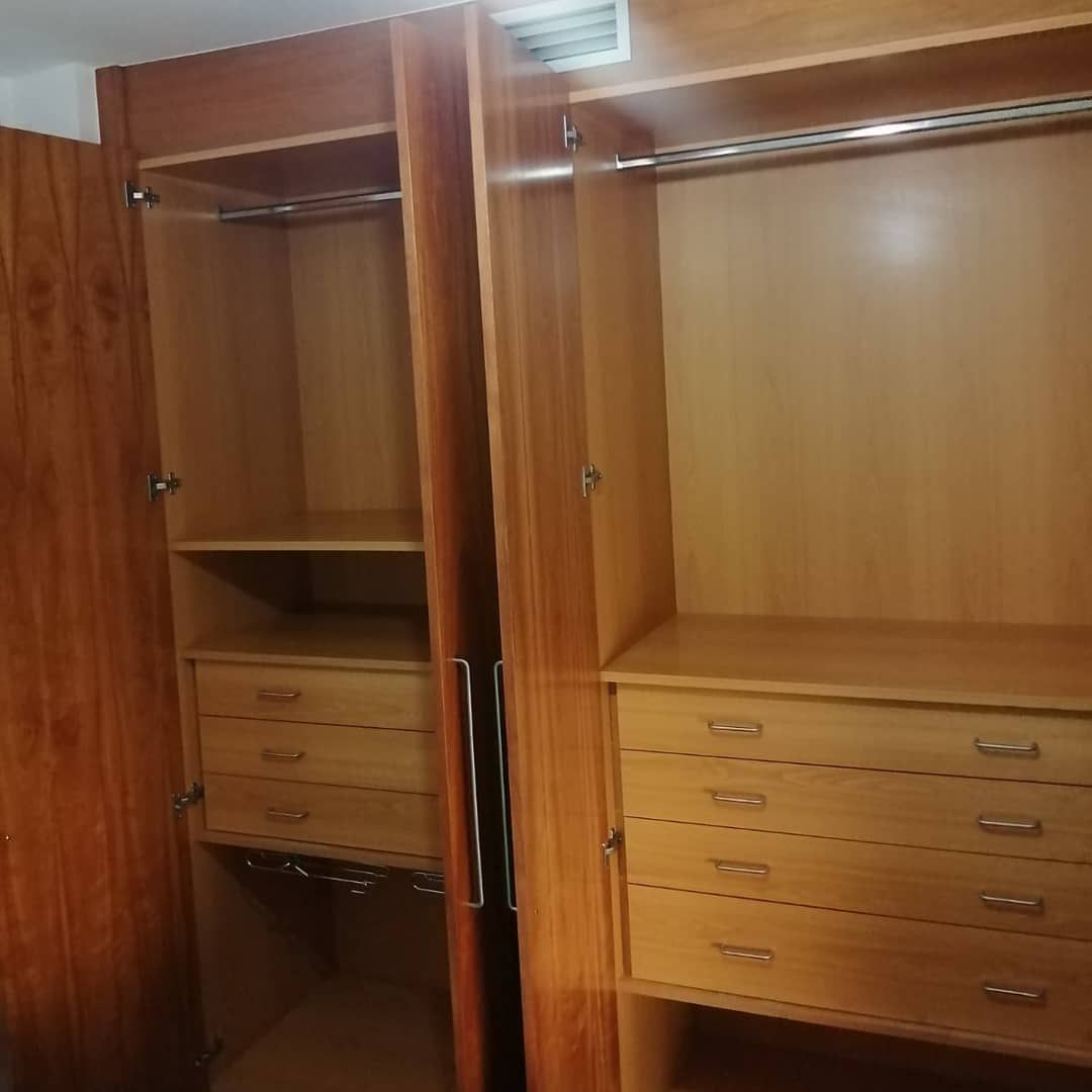 Armario de madera con puertas abiertas, mostrando estantes, cajones y barras para colgar.