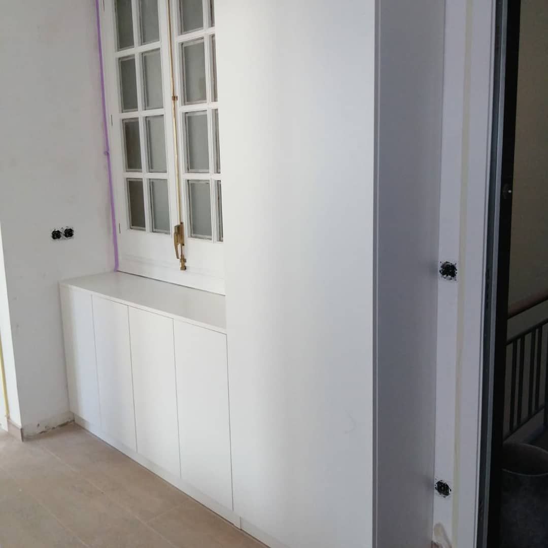 Armarios blancos bajo una ventana con marco de vidrio multicapa. Puerta abierta con escalera.