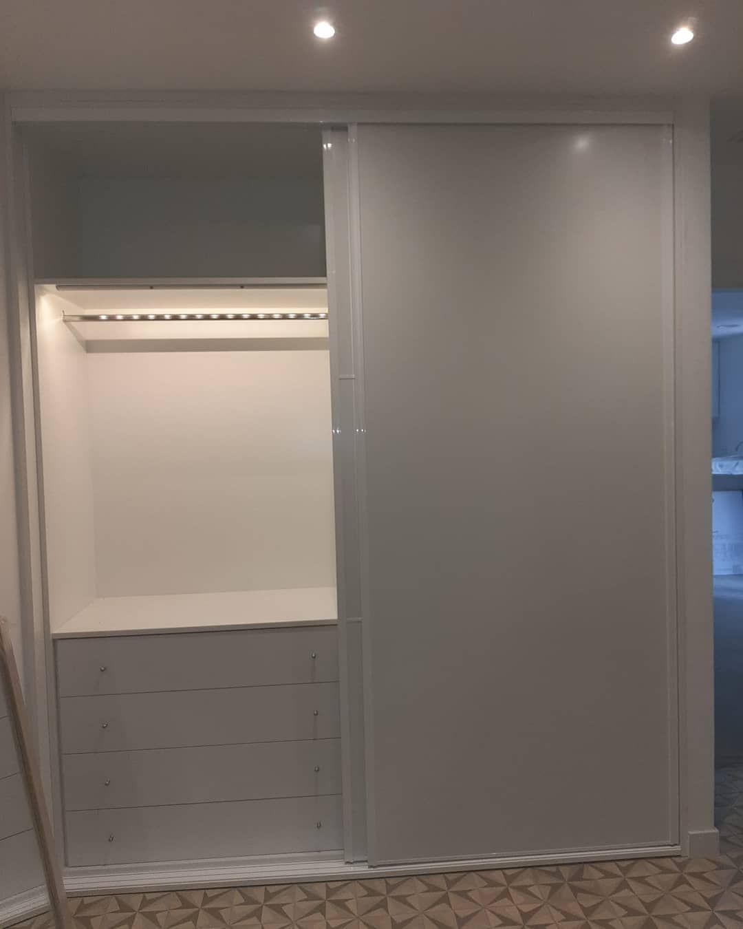 Armario empotrado blanco con puerta corrediza parcialmente abierta, que deja ver barra para colgar