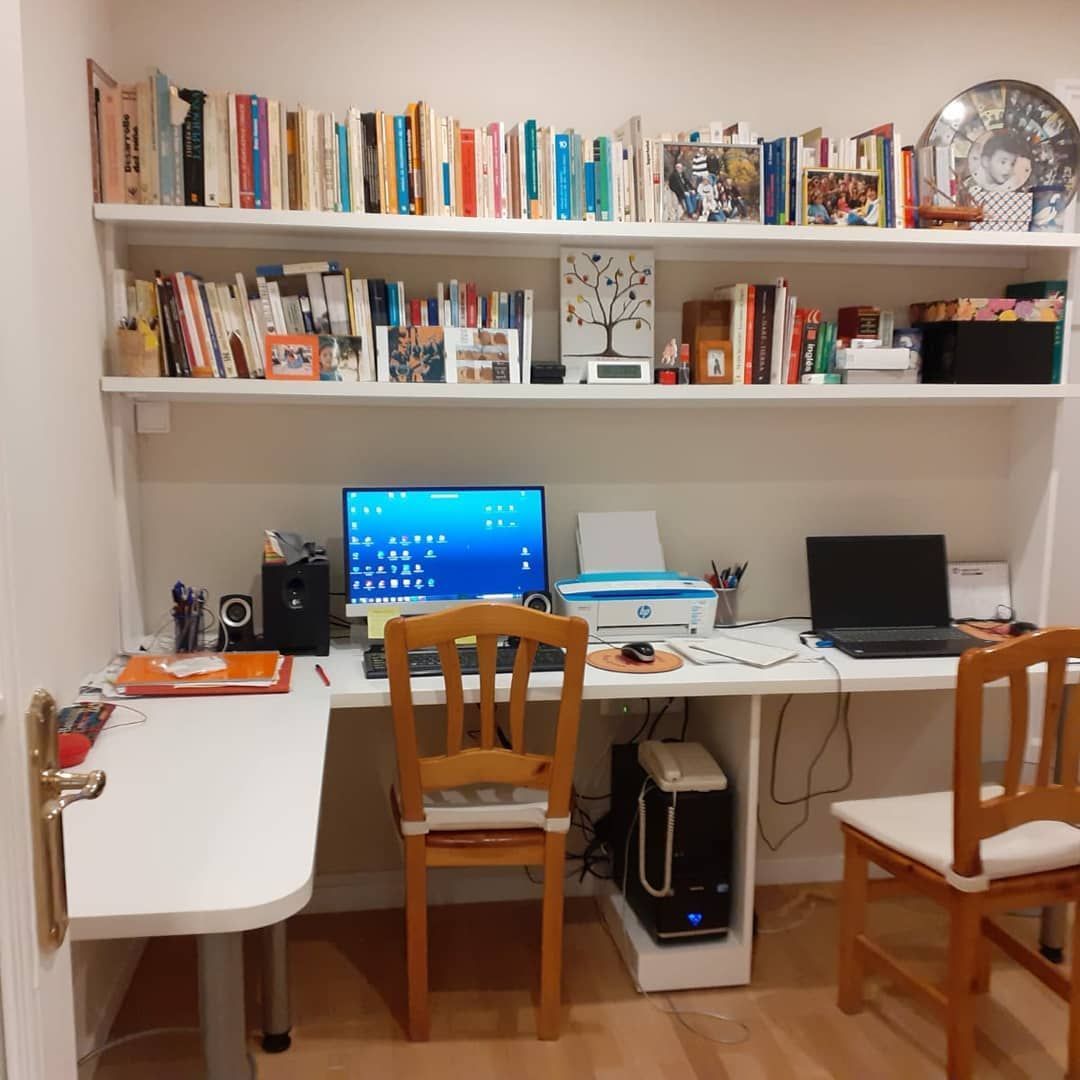 Oficina en casa con un escritorio, dos sillas, computadora, impresora y estanterías llenas de libros.