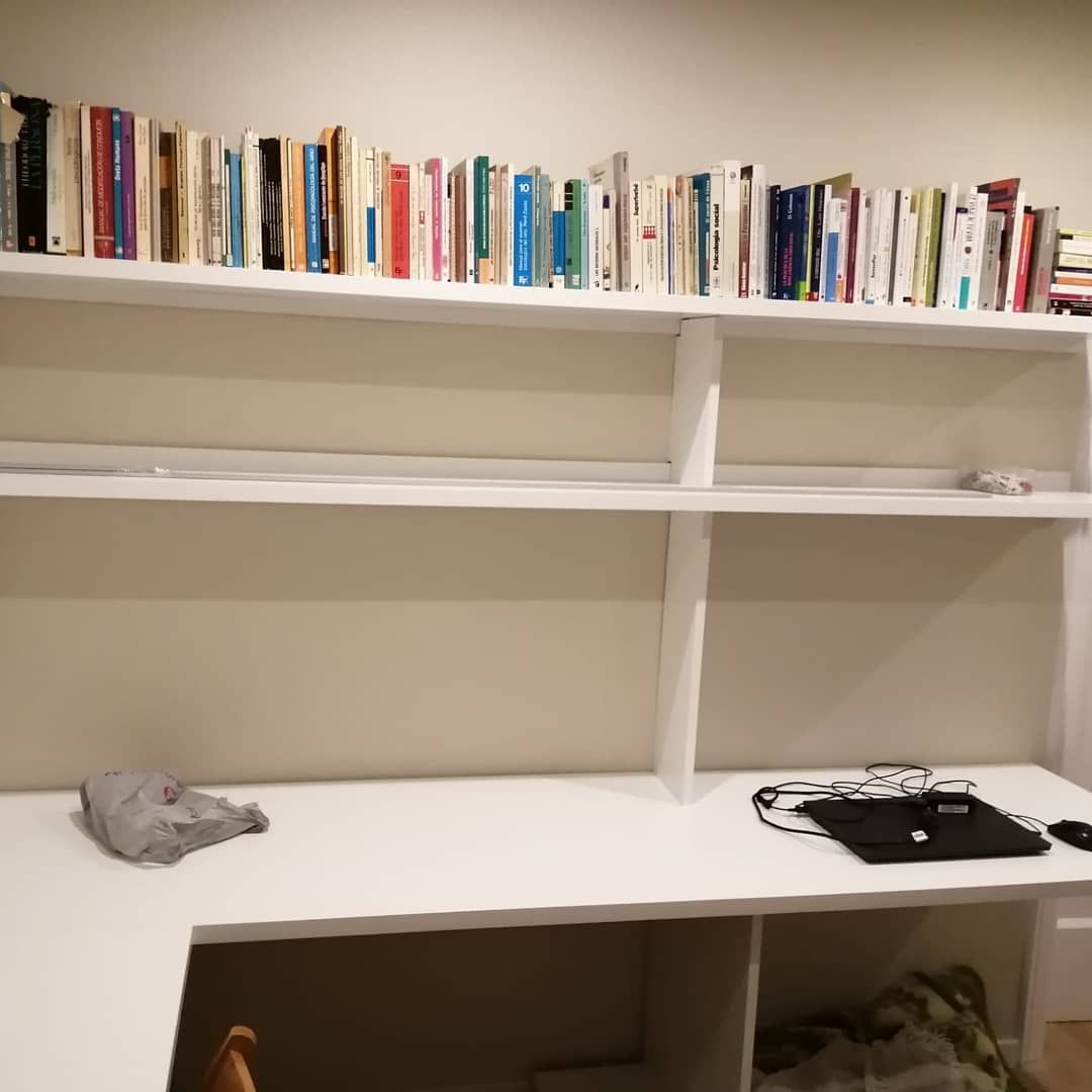 Escritorio blanco y estantes con una fila de libros en el estante superior.