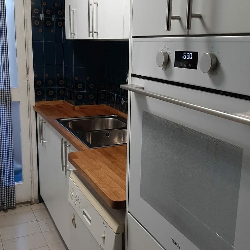 Pequeña cocina con gabinetes blancos, encimeras de madera y horno blanco.