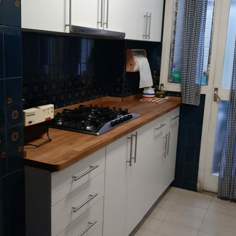 Gabinetes de cocina blancos con encimeras de madera, estufa negra y protector contra salpicaduras de azulejos azules.