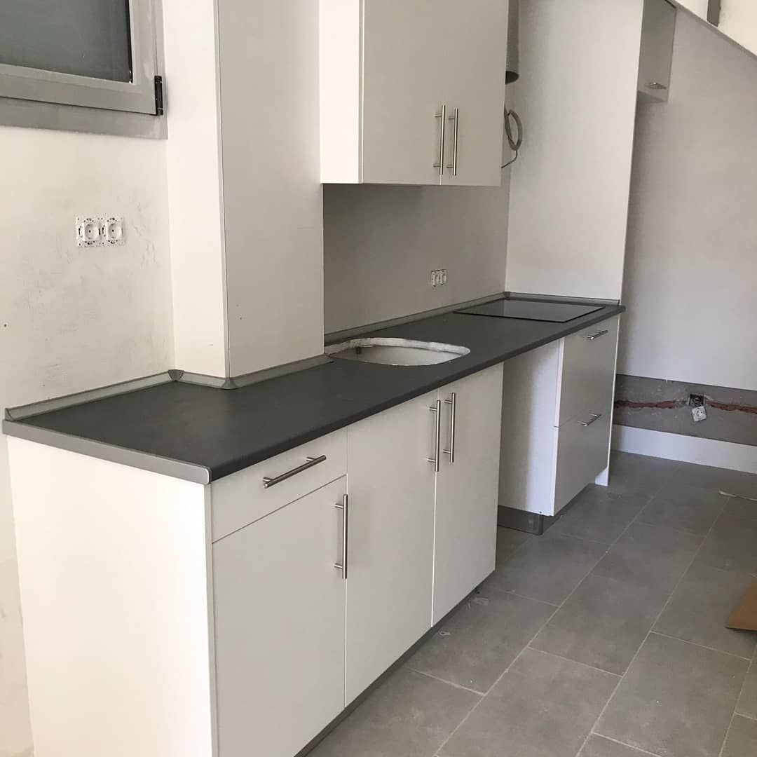 Gabinetes de cocina blancos con encimera oscura y manijas de acero inoxidable, empotrados en una pared blanca.